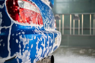 Temizlik köpüğünün altında, oto yıkama servisinin içinde kapalı mavi bir araba.