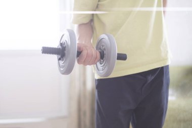 Kişi birkaç dambıl teçhizatıyla evde egzersiz yapıyor.