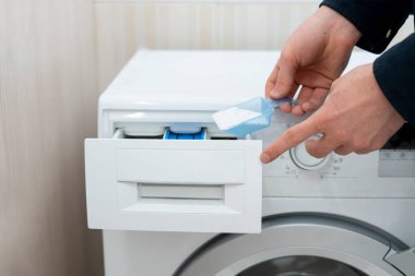 İnsan çamaşır deterjanını makineye doldurur.