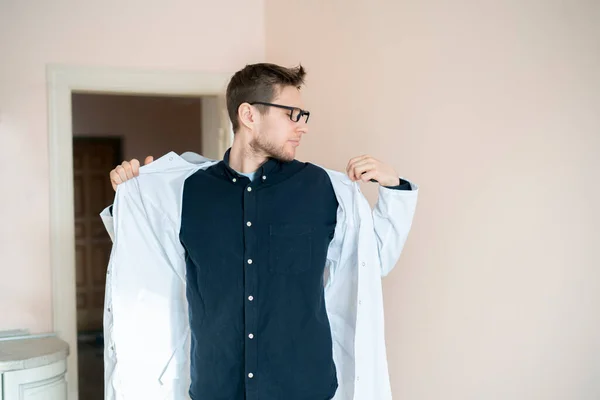 Um médico masculino colocar o uniforme vestido médico no hospital, clínica jovem especialista — Fotografia de Stock