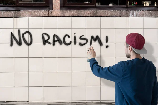Uma pessoa masculina escrever com tinta spray pode parar nenhuma declaração de racismo na parede, conceito de símbolo de grafite — Fotografia de Stock