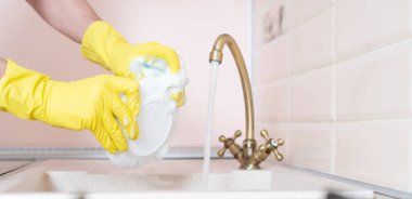 Kirli tabakları tutan elleri mutfak lavabosunda yıkıyor ve su döküyor.