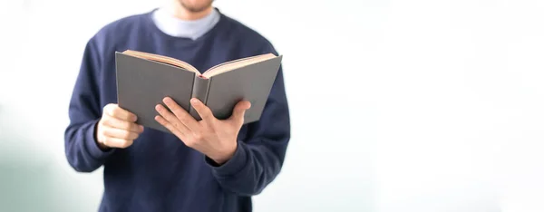 Un joven sosteniendo un libro, leyendo y obtener conocimiento de pie cerca de la pared, aislado — Foto de Stock