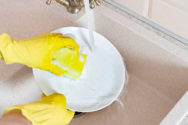 Um mãos segurando prato sujo e lave-o na pia da cozinha derramando água — Fotografia de Stock