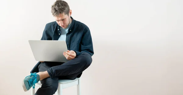 Joven hombre que trabaja en casa con el ordenador portátil, estilo de vida freelancer en línea sentado cerca de la pared aislado — Foto de Stock