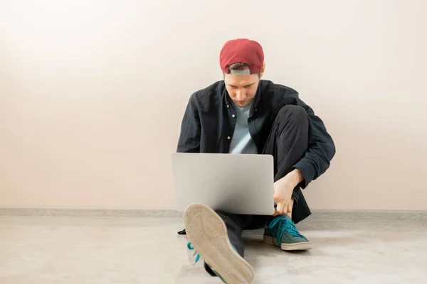 Joven hombre que trabaja en casa con el ordenador portátil, estilo de vida freelancer en línea sentado cerca de la pared aislado — Foto de Stock