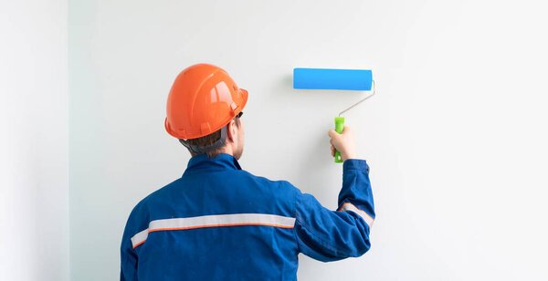 a worker painter painting the wall surface with a roller, man at work decorating a room