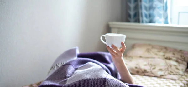 Une main levée de la personne au lit tenant une tasse de thé tôt le matin — Photo