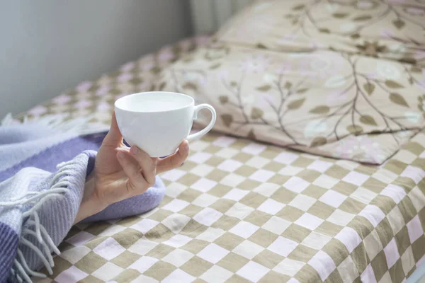 Поднятая рука человека в постели с чашкой чая ранним утром — стоковое фото