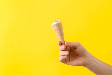 Renkli pastel arka planda izole edilmiş dondurma külahını tutan bir insan eli.