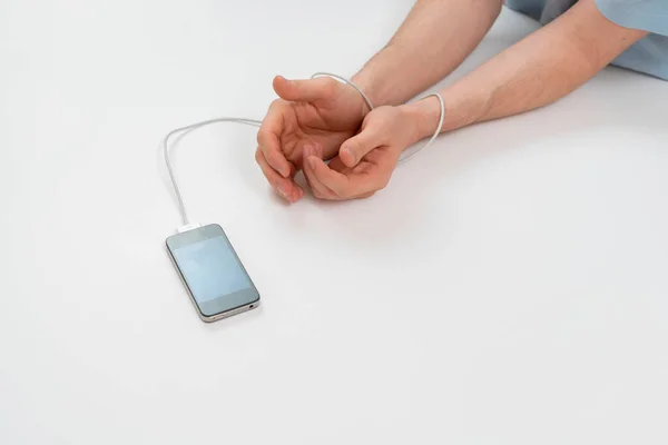 A person hands addicted to the digital mobile phone device, wire tied to arm — Stockfoto