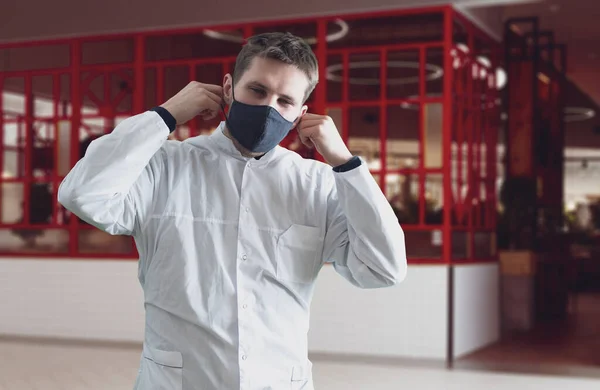 Um jovem médico do sexo masculino de uniforme usando a máscara protetora no hospital, clínica de medicina — Fotografia de Stock