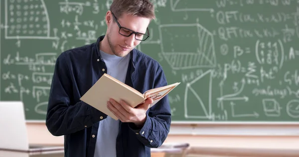 Un joven profesor en la universidad sosteniendo un libro en el aula — Foto de Stock
