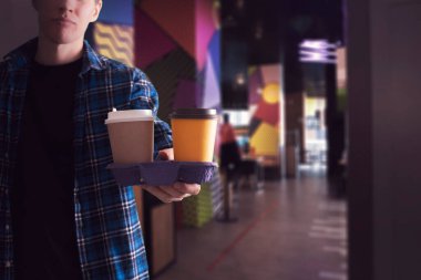 Elinde bir tepsi, elinde de birkaç kahve bardağı tutan bir adam.