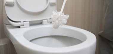 Bir el fırça tutuyor ve tuvaleti temizliyor.