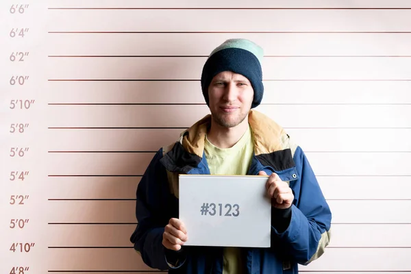 The arrested prisoner young man holding a placecard in front of the height chart — Stockfoto