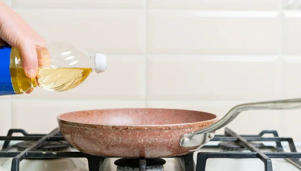 Une main de femme verser de l'huile de cuisson sur la casserole à la maison — Photo
