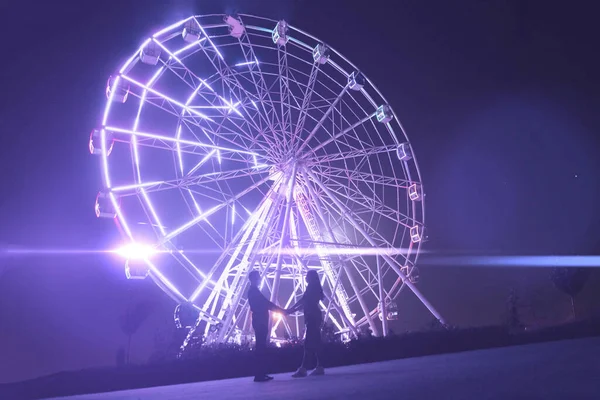 Um jovem homem e mulher romance amor na noite no parque de diversões perto da roda gigante — Fotografia de Stock