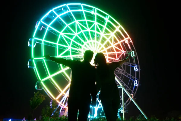 Um jovem homem e mulher romance amor na noite no parque de diversões perto da roda gigante — Fotografia de Stock