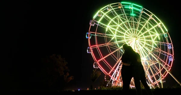 Um jovem homem e mulher romance amor na noite no parque de diversões perto da roda gigante — Fotografia de Stock