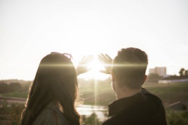 Bir çift genç adam ve kadın gökyüzünü seyrediyor ve güneşi ellerle örtüyor, güneş ışığı güzelliği