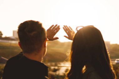 Bir çift genç adam ve kadın gökyüzünü seyrediyor ve güneşi ellerle örtüyor, güneş ışığı güzelliği