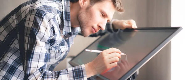 a young male digital artist drawing paint on the computer screen monitor in studio