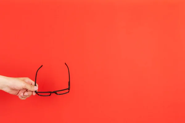 Una mano sosteniendo gafas negras aisladas contra el fondo colorido, minimalismo concepto simple — Foto de Stock