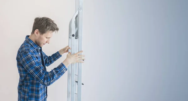 Рабочий держит алюминиевую лестницу напротив стены в новом доме — стоковое фото