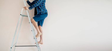 İşçi ayaklarıyla merdivenin tepesine tırmanıp duvara tırmanmak.