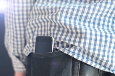 Erkek kıyafetlerinin cebinde yakın plan akıllı telefon, cep telefonunun sağlık etkilerinin sembolü olarak arka plan.