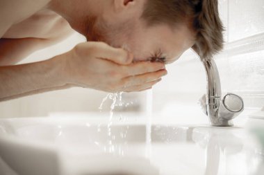 Genç sakallı adam her sabah banyodaki lavaboya su sıçratarak yüzünü yıkıyor.