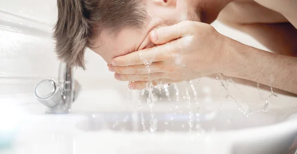 Fiatal szakállas férfi mossa arcát fröccsenő a mosdóban, minden reggel rutin — Stock Fotó