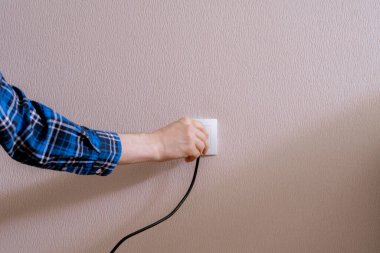 Bir el elektrik kablosunu tutuyor ve evdeki duvarın içine yerleştiriyor.