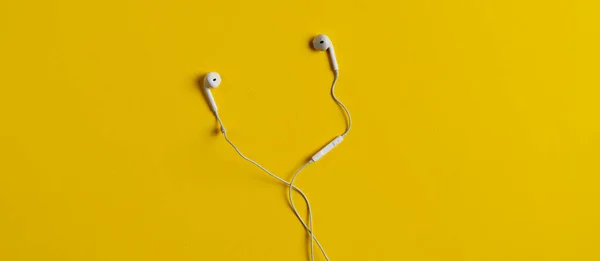 A view from above of the white wired simple earbuds earphones flat lay on the colorful background isolated wide long banner — Stock Photo, Image