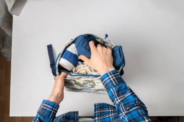 Bir insan eli sırt çantasına bazı şeyler ve malzemeler koyar. Masanın renkli yüzeyine. Basit bir başlangıç yolculuğu kavramı.