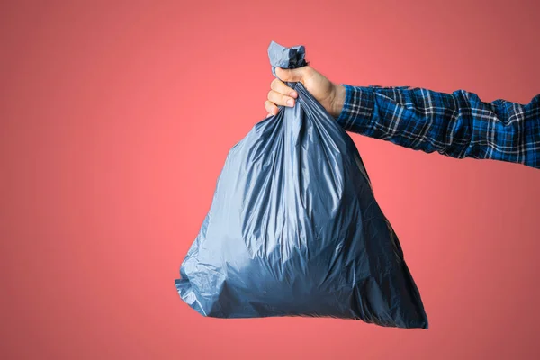 Una mano sosteniendo la bolsa de basura azul oscuro, concepto de limpieza del planeta tierra, aislado contra la pared de color, concepto simple — Foto de Stock