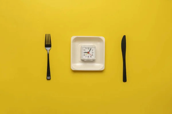 Un concepto simple con el reloj en plato blanco, tenedor y cuchillo plano yacía en la mesa de colores, su tiempo de dieta, detener el sobrepeso —  Fotos de Stock