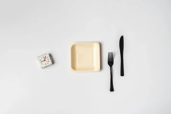 Un concepto simple con el reloj en plato blanco, tenedor y cuchillo plano yacía en la mesa de colores, su tiempo de dieta, detener el sobrepeso —  Fotos de Stock