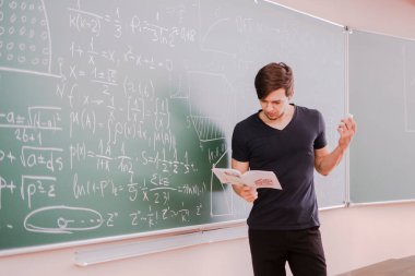 Üniversitede tahtanın yanında duran ve matematik denklemini düşünen genç bir öğrenci.