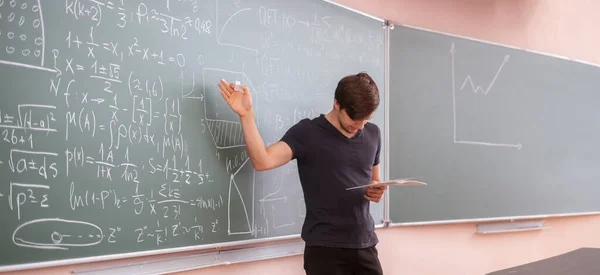 Um jovem estudante na universidade de pé ao lado do quadro negro e pensando na equação da matemática — Fotografia de Stock