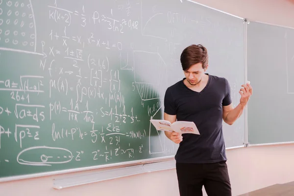 Un joven estudiante en la universidad de pie junto a la pizarra y pensando en la ecuación de matemáticas — Foto de Stock