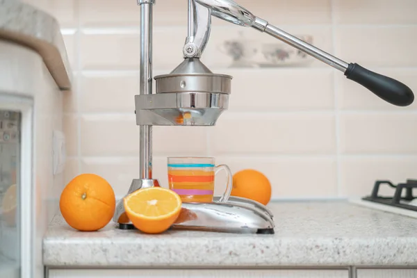 Stalen metalen handpers sappers met gesneden sinaasappels en glas op de keukentafel thuis — Stockfoto