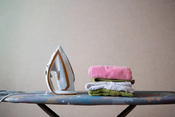 Una escena simple de la plancha y la pila de toallas coloridas limpias frescas en la tabla de planchar en casa — Foto de Stock