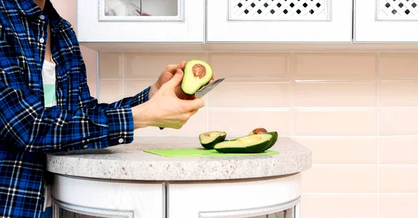 Ręka z nożem przeciętym awokado na desce w kithcen w domu — Zdjęcie stockowe