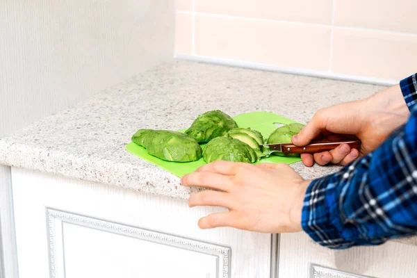 Een hand met een mes gesneden avocado op het bord in de kithcen thuis — Stockfoto