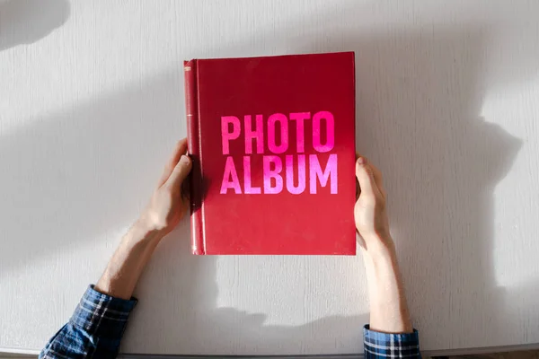 Una vista aérea de las manos de las personas que sostienen el libro rojo álbum de fotos, nostalgia familiar — Foto de Stock