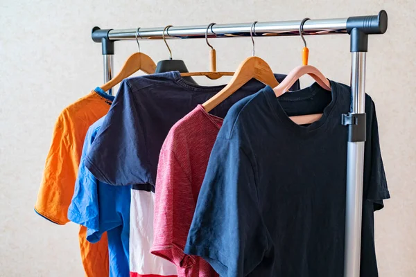 Un conjunto simple de camisetas de colores en una percha en casa cerca de la pared, concepto minimalista simple — Foto de Stock