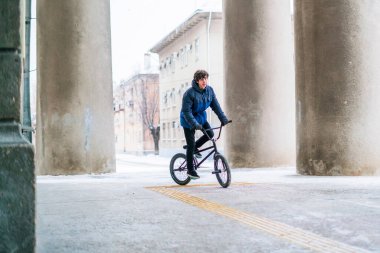 Genç erkek B sütunları arasında çatısı altında kara bulutlu bir günde siyah bmx sürüyor.