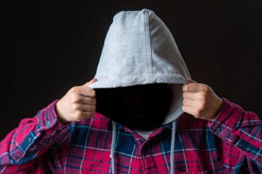 Kimliği belirsiz bir adam karanlık arka planda başlık takıyor.